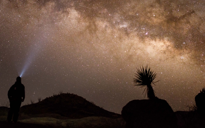 the silhouette of a person wearing a headlamp is illuminated against a starry night sky